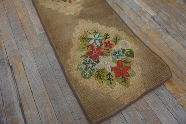 A tan looped runner rug with multicolored floral designs rests on distressed gray wood plank flooring.