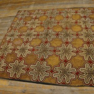 Textured rug with repeating brown, red, and beige star motifs on a gold field, lying on distressed wood planks.
