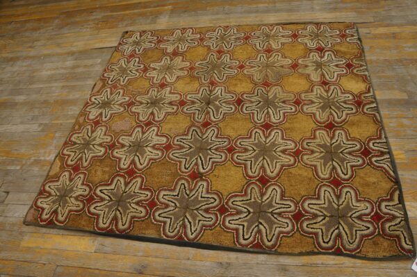 Textured rug with repeating brown, red, and beige star motifs on a gold field, lying on distressed wood planks.