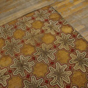 Gold hooked rug with repeating brown and red floral patterns on distressed wood floor.