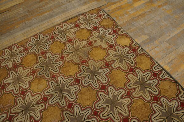 Gold hooked rug with repeating brown and red floral patterns on distressed wood floor.