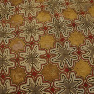 Textured gold rug with repeating brown, gray, red, and cream stylized floral patterns next to wood flooring.