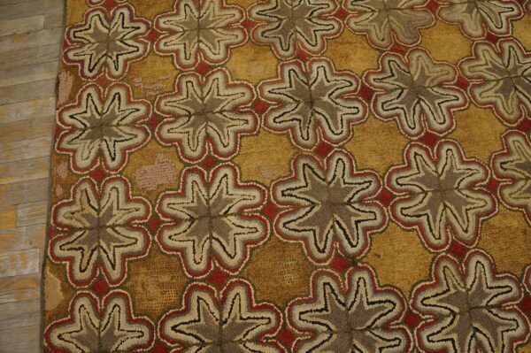 Textured gold rug with repeating brown, gray, red, and cream stylized floral patterns next to wood flooring.