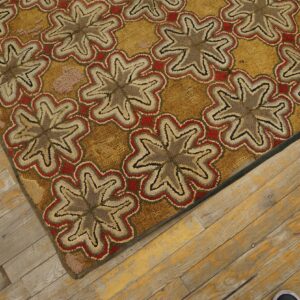 Tan, red, and brown hooked rug with repeating floral medallions lies diagonally on distressed wood flooring.