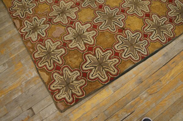 Tan, red, and brown hooked rug with repeating floral medallions lies diagonally on distressed wood flooring.