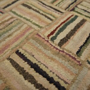 Muted beige, pink, green, and dark striped low-pile rug arranged in a diagonal block pattern.