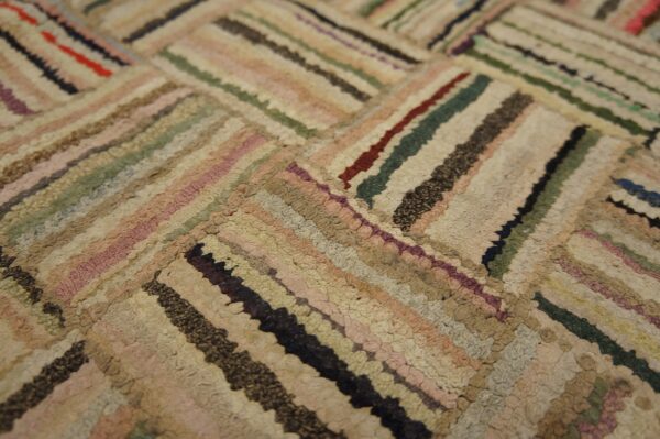 Muted beige, pink, green, and dark striped low-pile rug arranged in a diagonal block pattern.