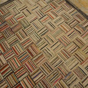 A textured, multicolored rag rug with a striped herringbone pattern rests on distressed light wood planks.