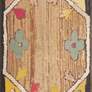 Rustic hooked rug with a central beige diamond pattern bordered by stylized maroon and yellow flowers.