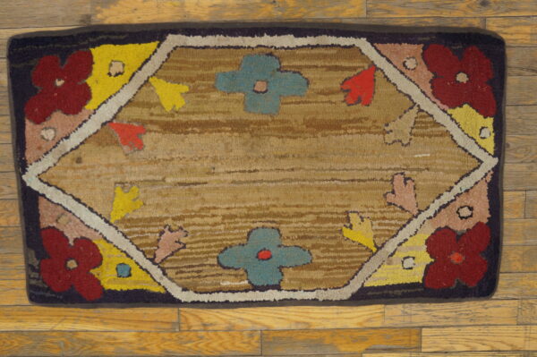 Low pile hooked rug featuring red, blue, and yellow floral patterns on a light tan field and wood flooring.