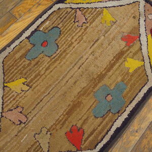 A rectangular, textured rug with colorful floral motifs on a brown background rests on hardwood flooring.