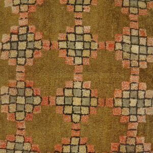 High-pile shag rug featuring a geometric block pattern in rust, tan, and moss green over pale wooden planks.
