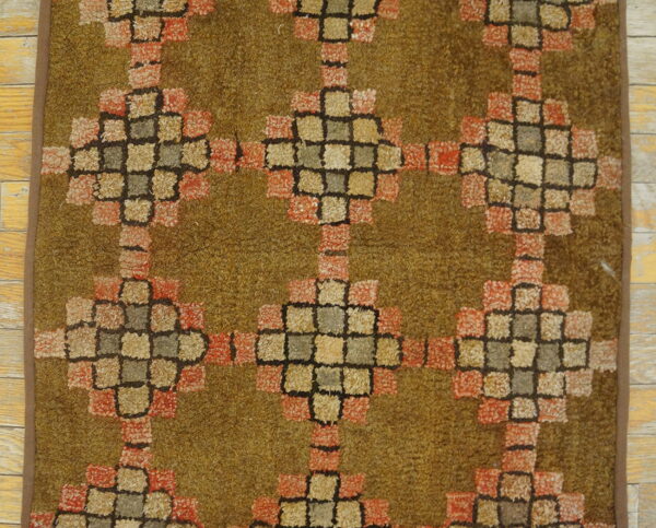 High-pile shag rug featuring a geometric block pattern in rust, tan, and moss green over pale wooden planks.