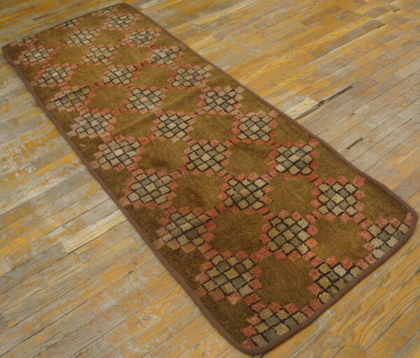 Olive-brown runner rug with a geometric lattice design sits on distressed yellow and gray wood flooring.