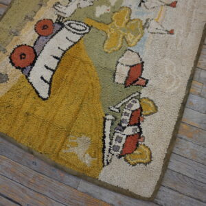 A colorful hooked rug with stylized shapes in yellow, olive, and rust sits on distressed gray plank flooring.