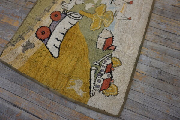 A colorful hooked rug with stylized shapes in yellow, olive, and rust sits on distressed gray plank flooring.