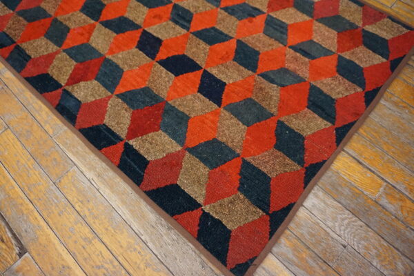 Geometric rug with red, tan, and dark blue 3d cube pattern on distressed wood planks.