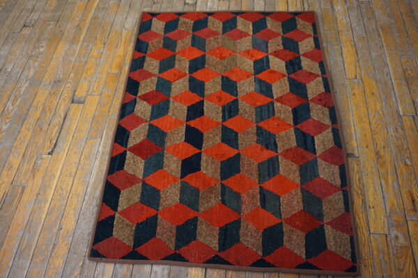 Low-pile rug with red, teal, and brown tumbling cubes rests on worn yellow wood flooring.