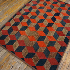 Red, teal, and brown geometric cube pattern rug rests on worn, light brown wood plank flooring.