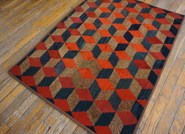 Red, teal, and brown geometric cube pattern rug rests on worn, light brown wood plank flooring.