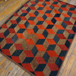 A textured rug with red, dark blue, and tan tumbling block cubes sits on distressed wood flooring.