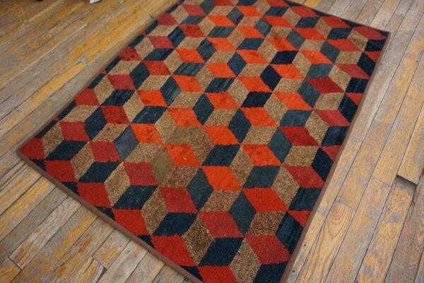 A textured rug with red, dark blue, and tan tumbling block cubes sits on distressed wood flooring.