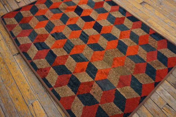Textured rug with interlocking cubes pattern in orange, dark blue, and tan on weathered wood flooring.