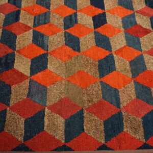 Orange, navy, and brown coarse rug displaying a geometric cube illusion pattern on light wood floor.