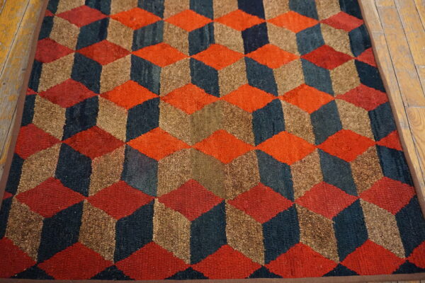Orange, navy, and brown coarse rug displaying a geometric cube illusion pattern on light wood floor.