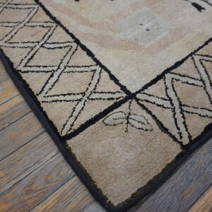 High-pile beige rug with black geometric borders and a leaf detail rests on rustic wood floorboards.