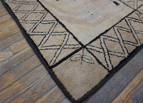 High-pile beige rug with black geometric borders and a leaf detail rests on rustic wood floorboards.