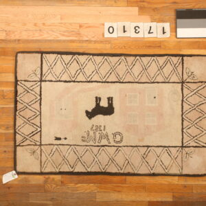 A light-colored hooked rug with black border and folk art motifs rests on hardwood flooring.