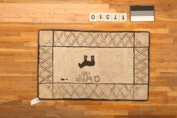 A light-colored hooked rug with black border and folk art motifs rests on hardwood flooring.