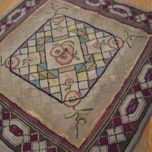 Muted tan rug featuring a central pink floral diamond and a wide maroon and brown geometric border on wood floors.