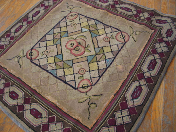 Muted tan rug featuring a central pink floral diamond and a wide maroon and brown geometric border on wood floors.