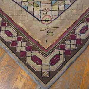 Textured rug corner with beige geometric field, floral vine details, and thick border featuring maroon and brown geometric shapes.