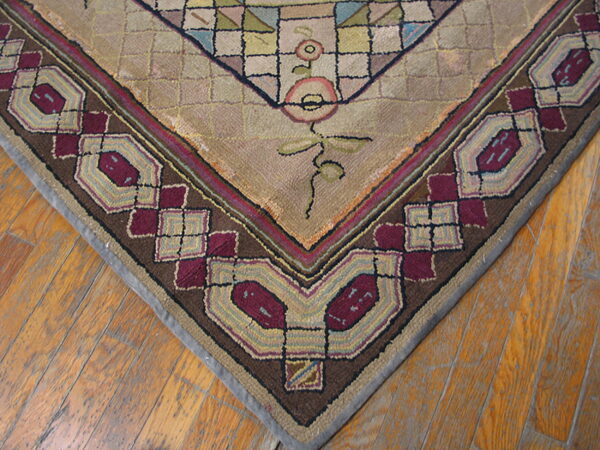 Textured rug corner with beige geometric field, floral vine details, and thick border featuring maroon and brown geometric shapes.
