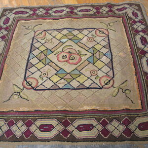 Tan geometric rug featuring a central pink fruit motif and burgundy border on a light brown wood floor.
