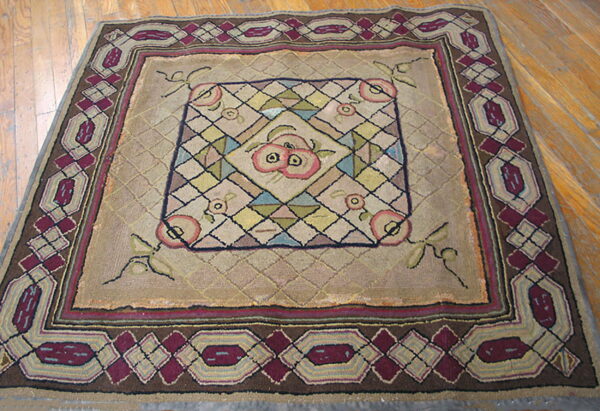 Tan geometric rug featuring a central pink fruit motif and burgundy border on a light brown wood floor.