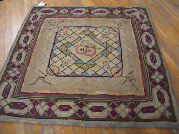 Tan rug with a central multi-color fruit motif and wide geometric borders on wood flooring.