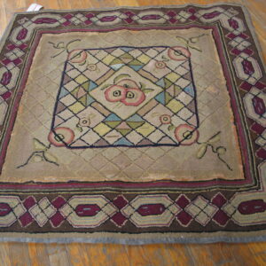 Square rug featuring a burgundy geometric border and central fruit pattern, lying on light brown wood flooring.