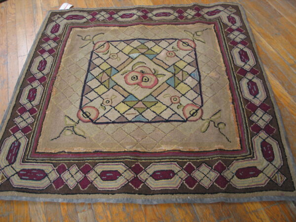 Square rug featuring a burgundy geometric border and central fruit pattern, lying on light brown wood flooring.
