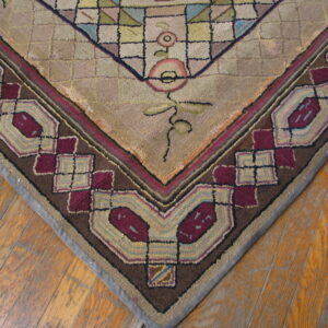 Textured rug corner in beige, dark brown, and maroon features geometric border on wood flooring.
