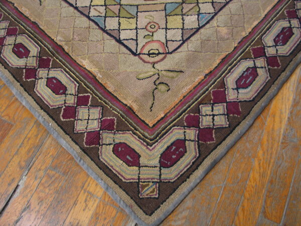 Textured rug corner in beige, dark brown, and maroon features geometric border on wood flooring.