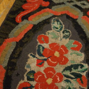 Textured loop pile rug featuring a bold coral and green floral design against dark charcoal on wood floors.