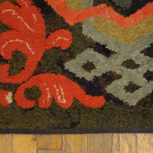 Textured rug corner showing stylized coral floral motifs and geometric designs on olive green.