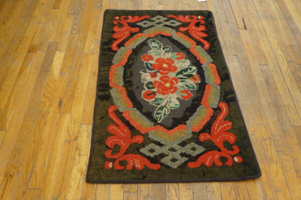 A dark green and red hooked rug with a floral medallion sits on a light honey-colored wood floor.