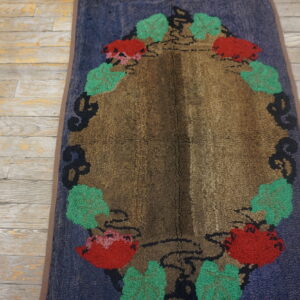 Oval textured rug with a brown center and red and green floral pattern on blue ground, lying on distressed wood.