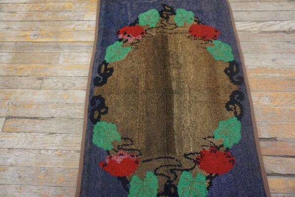 Oval textured rug with a brown center and red and green floral pattern on blue ground, lying on distressed wood.