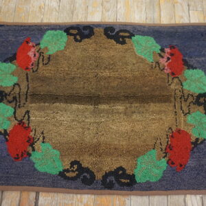 Looped pile rug in blue, brown, red, and green with a decorative fruit and leaf border on wood planks.